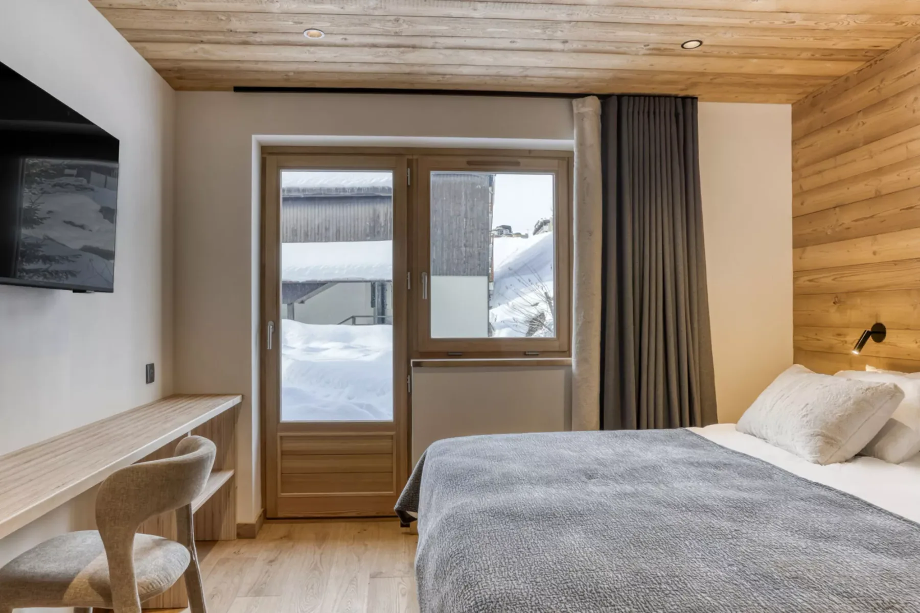 A bedroom with a bed beside a glass door and snowy mountain views.