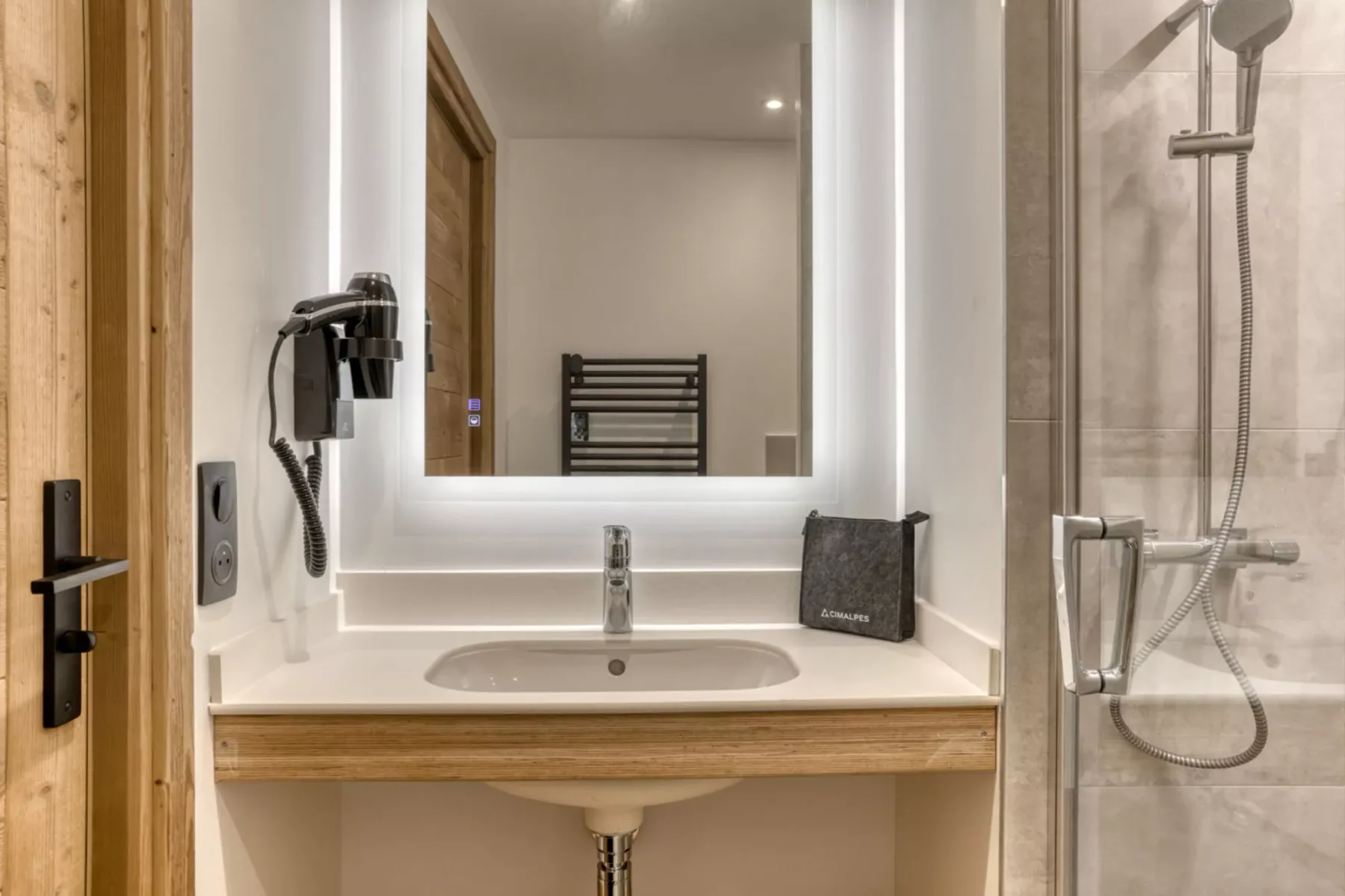 A bathroom vanity with a sink and illuminated mirror beside a glass shower.