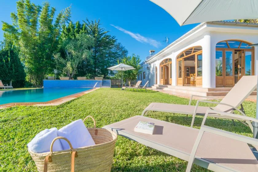Un césped soleado junto a la piscina, con tumbonas al lado de una casa blanca.