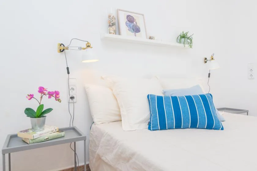 Un dormitorio luminoso con una cama, un cojín azul a rayas y una mesita de noche.