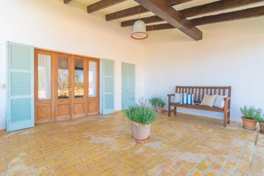 Un patio cubierto y luminoso con un banco de madera y suelo de baldosas.