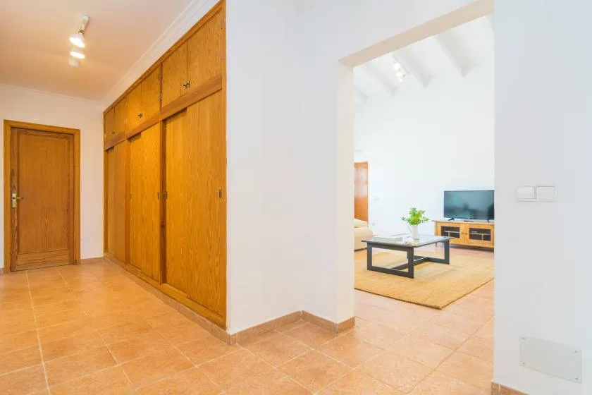 Un pasillo con suelo de baldosas y puertas de madera da a una sala luminosa.