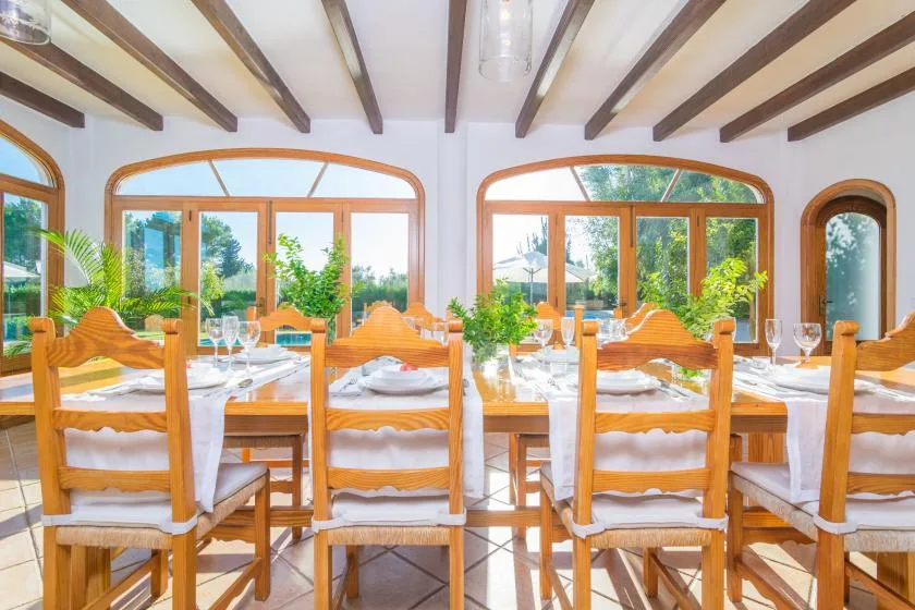 Un comedor con mesas y sillas de madera junto a grandes ventanas.