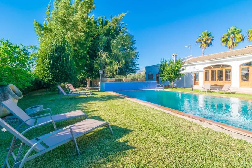 Una piscina junto a un césped y tumbonas al aire libre.