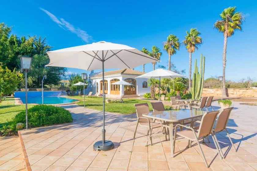 Un patio soleado con una mesa de comedor, sombrillas y una piscina.