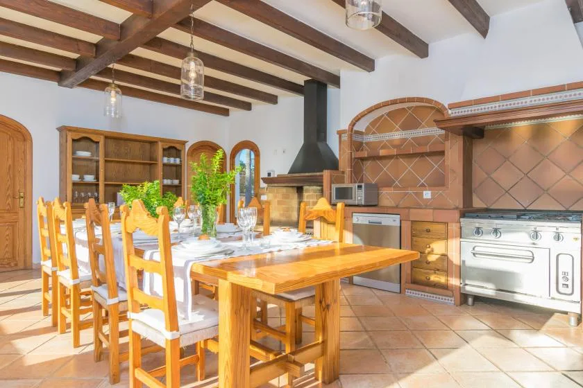 Una cocina y comedor luminosos con mesas de madera y vigas expuestas en el techo.