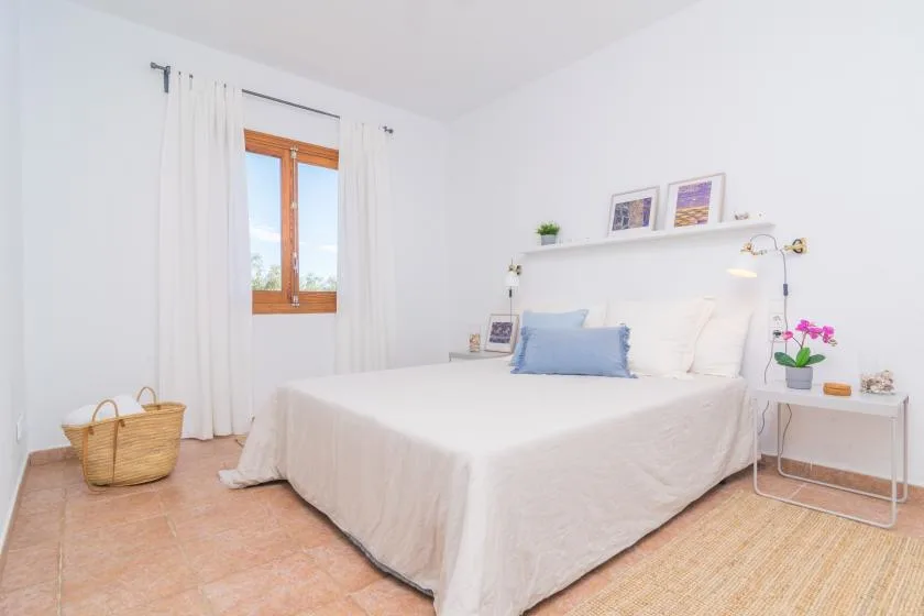 Un dormitorio luminoso con una cama bien arreglada y una ventana con cortinas blancas.