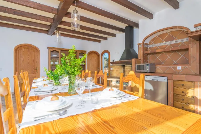 Comedor con una larga mesa de madera preparada para comer junto a una cocina.