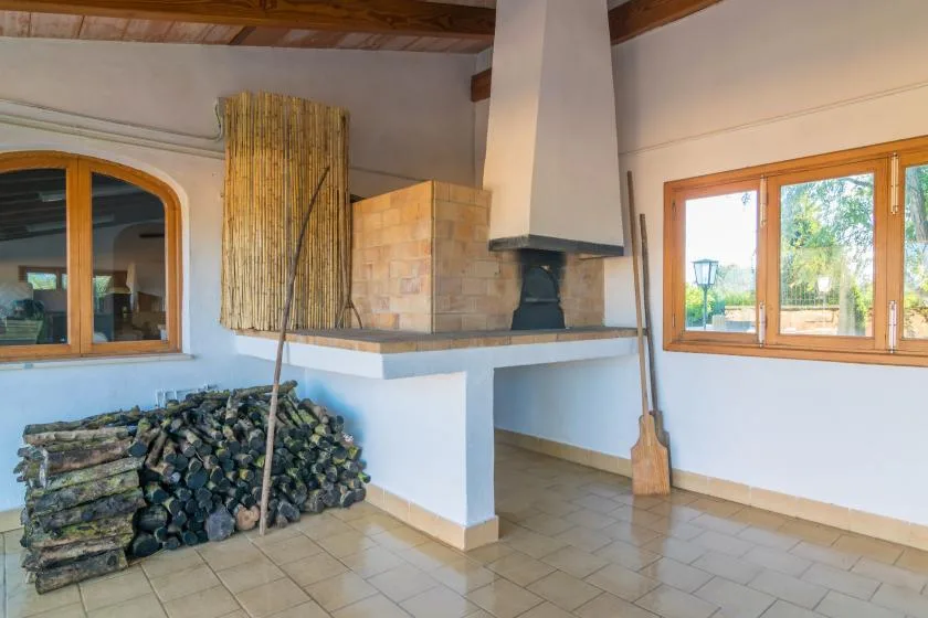Una zona interior luminosa con chimenea, leña apilada y ventanas.