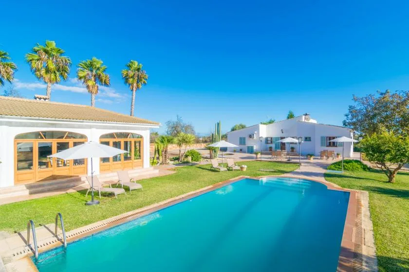 Una piscina al aire libre junto a un césped y edificios blancos.