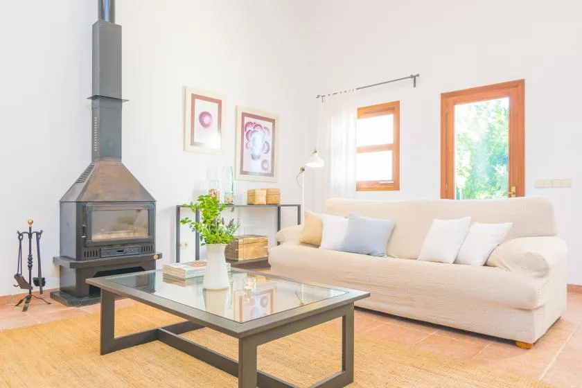 Una sala luminosa con un sofá claro, una mesa de centro de vidrio y una chimenea.