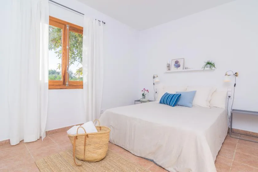 Un dormitorio luminoso con una cama, cortinas blancas y una ventana con marco de madera.
