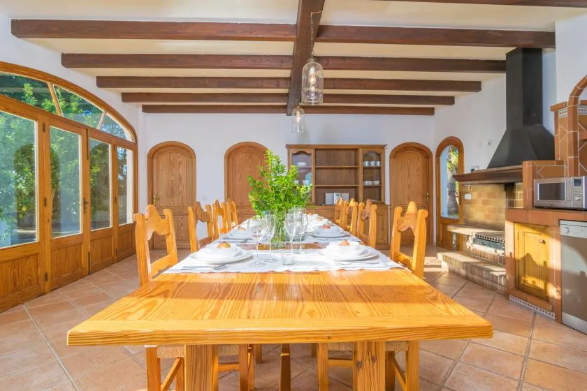 Un comedor con una larga mesa de madera y sillas bajo vigas de techo expuestas.
