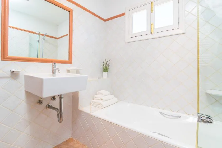 Un baño alicatado con lavabo de pared y bañera.