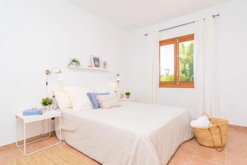 Un dormitorio luminoso con una cama bien hecha y una ventana enmarcada por cortinas blancas.
