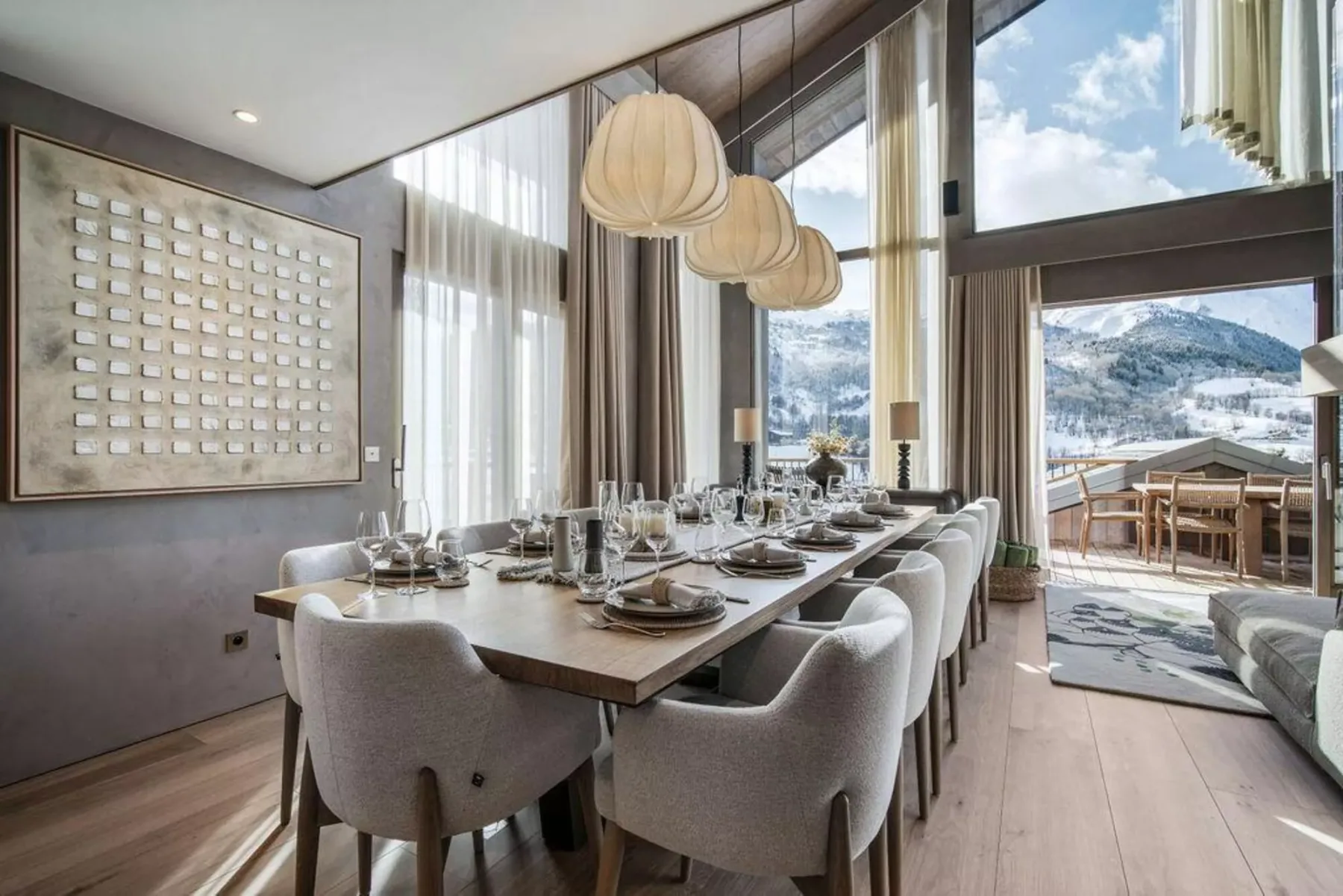 Comedor con una mesa larga y grandes ventanales que dan a un paisaje montañoso nevado.