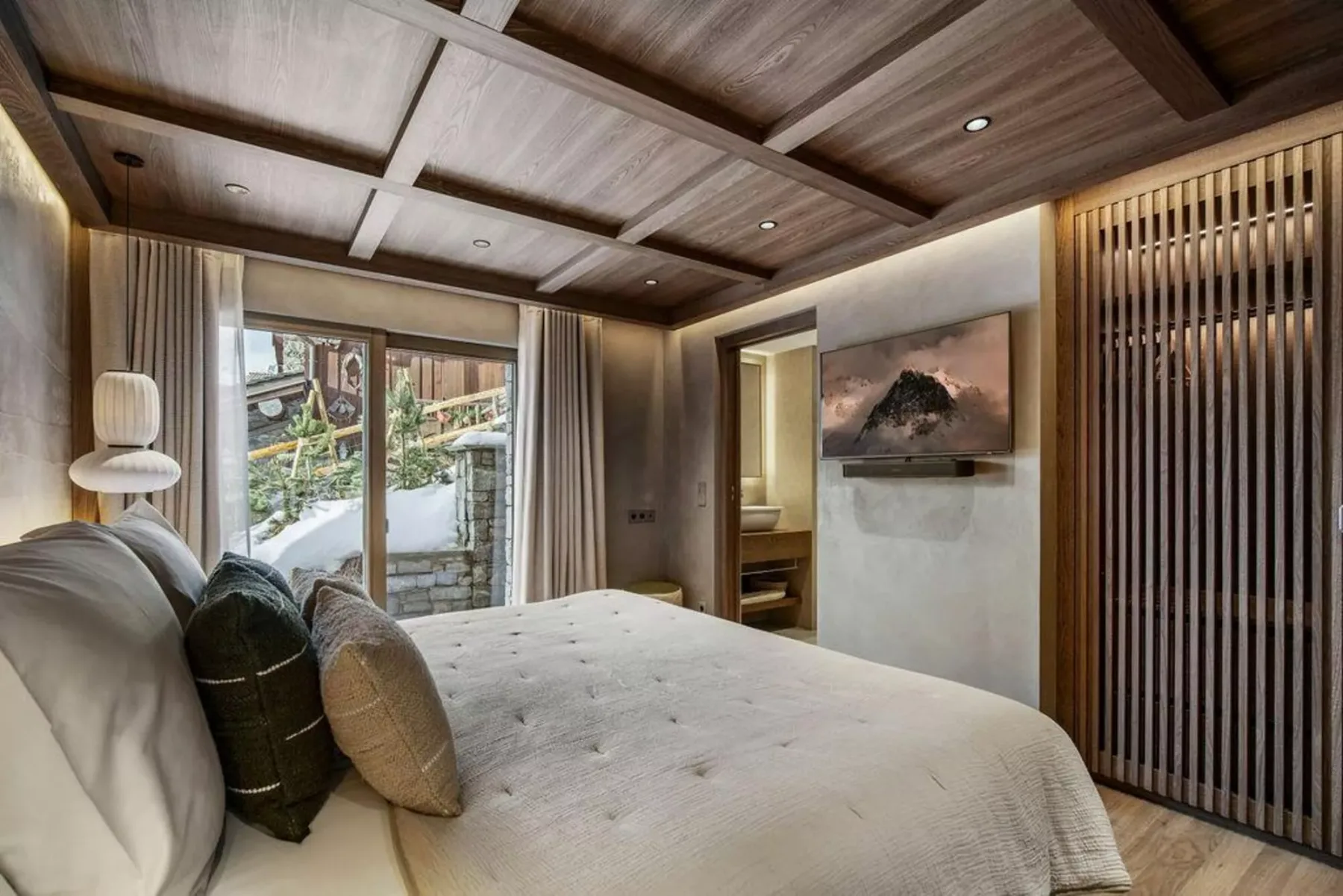 Un dormitorio con una cama, un televisor en la pared y ventanas grandes.
