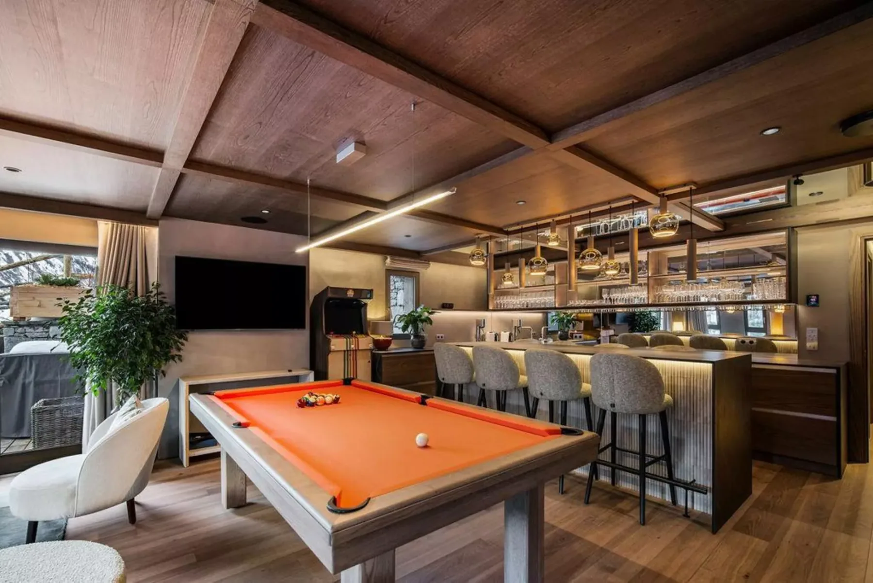 Una sala de juegos cuenta con una mesa de billar de paño naranja junto a una barra larga.