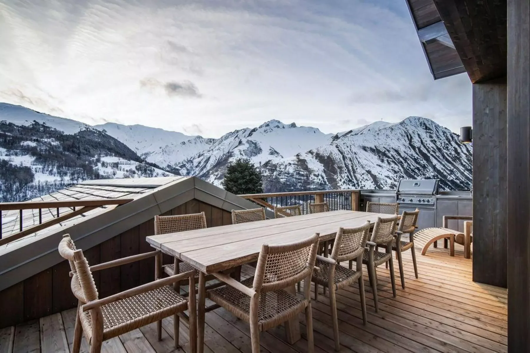 Una terraza de madera con asientos al aire libre tiene vistas a montañas nevadas.