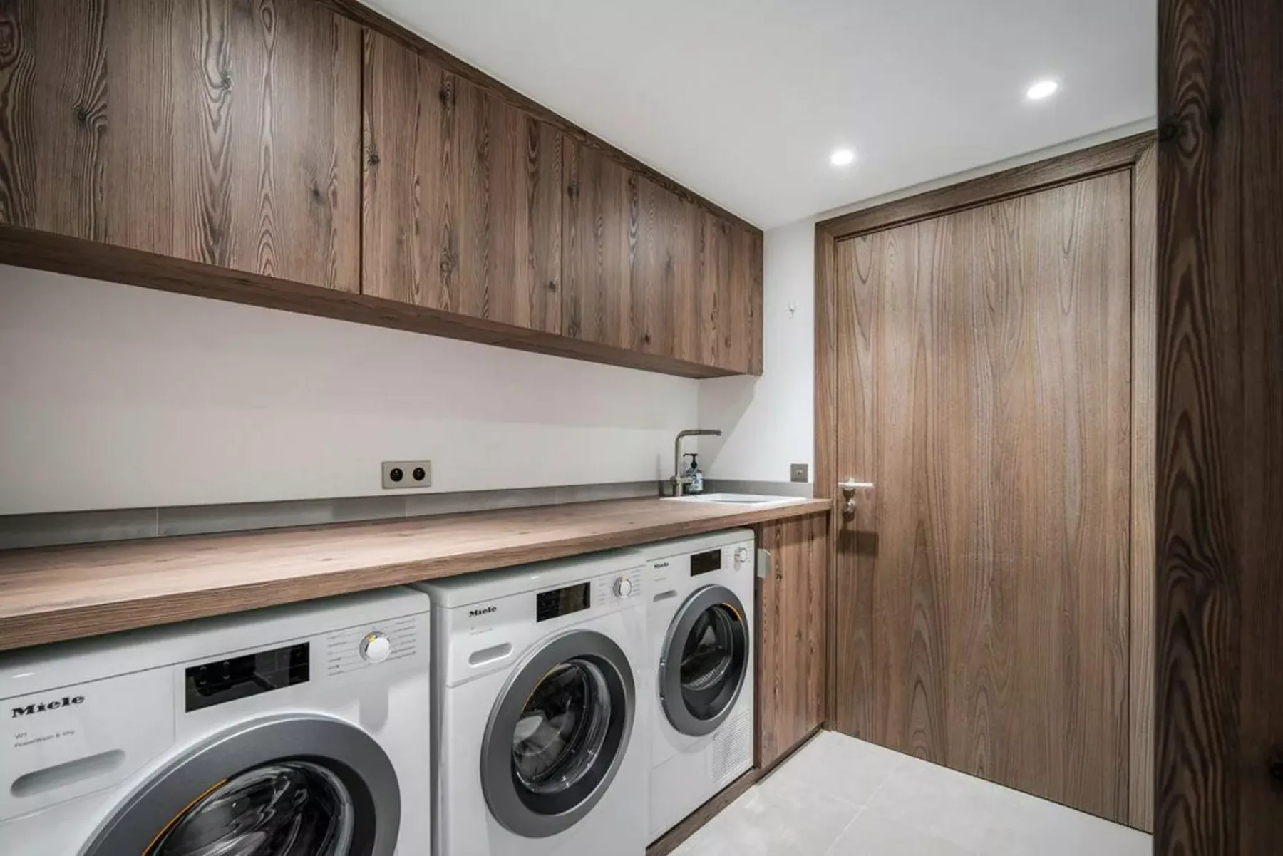 Un cuarto de lavandería con lavadoras debajo de armarios de madera.