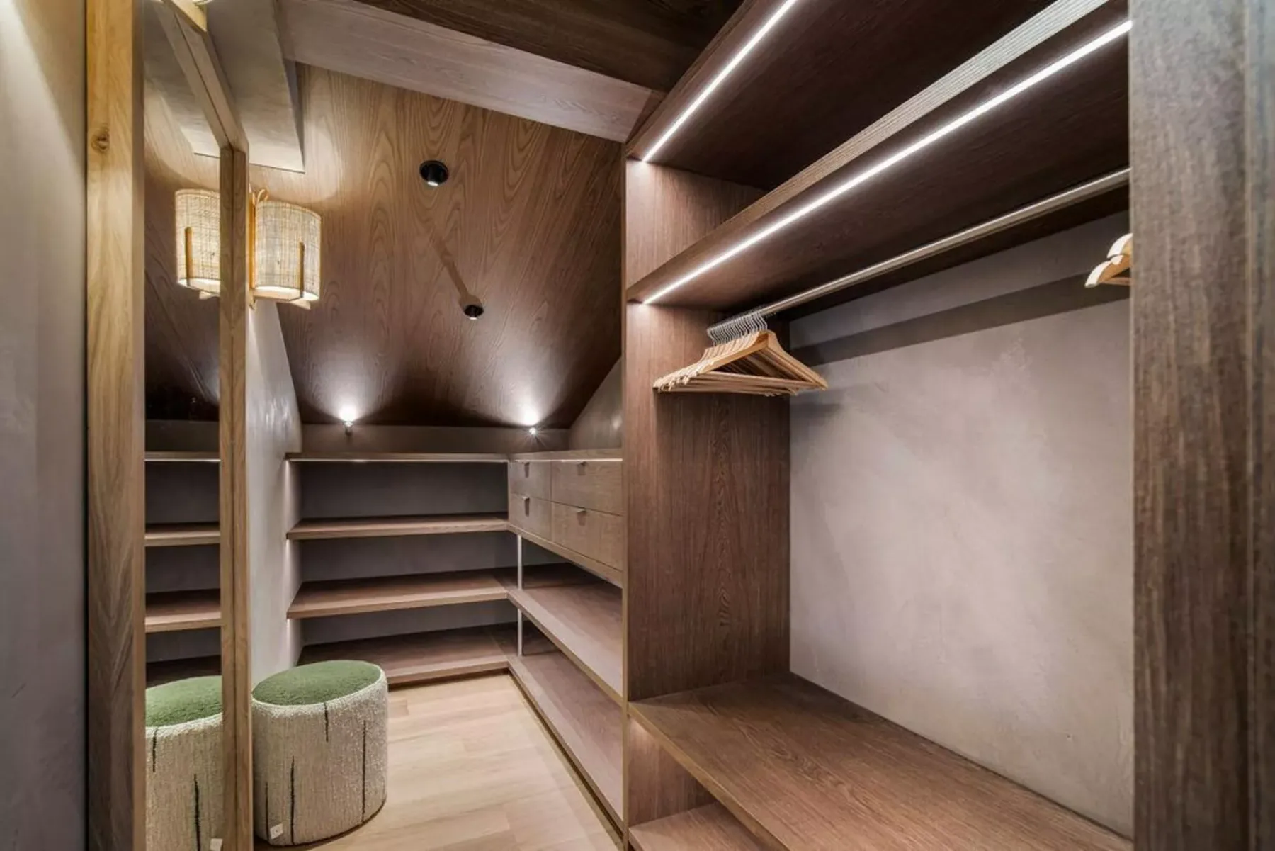Un vestidor con estantes abiertos, espacio para colgar ropa y un pequeño asiento tapizado.