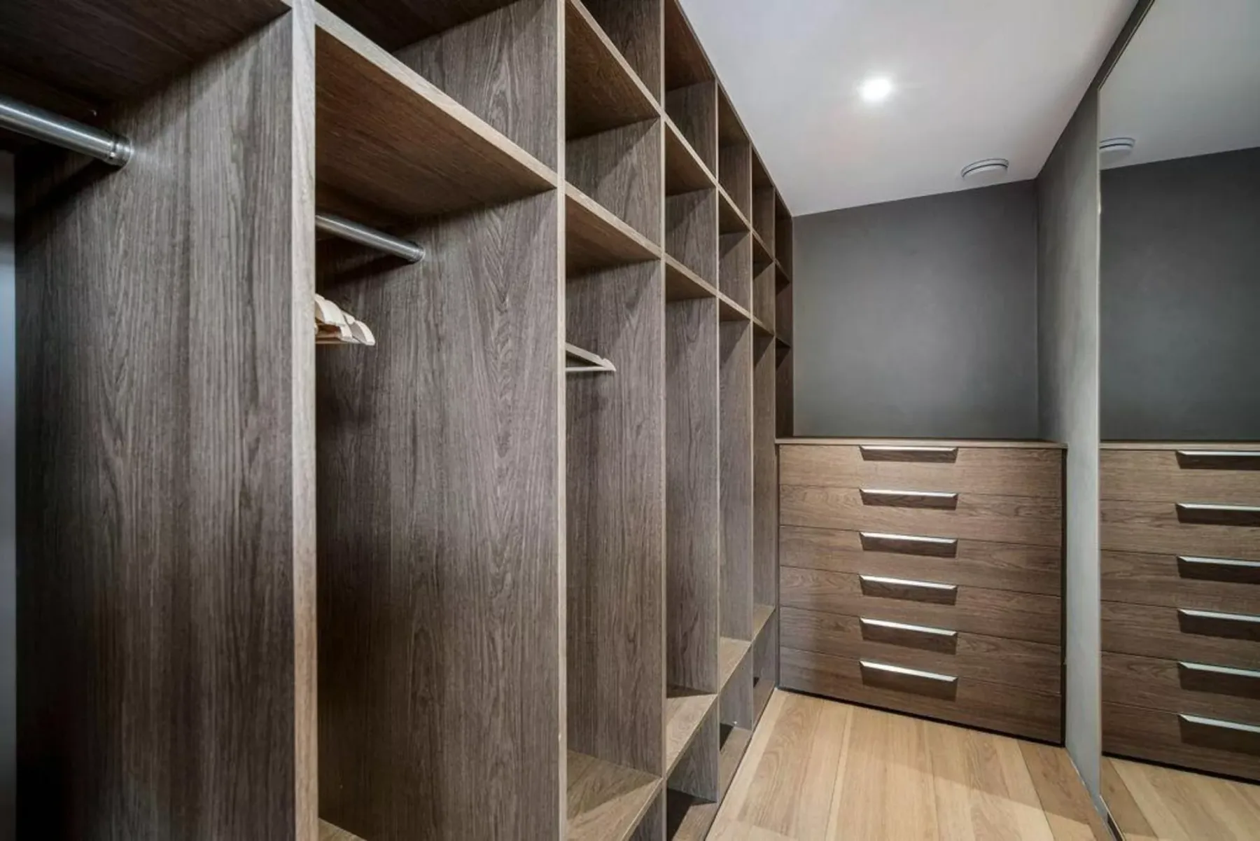 Un vestidor con estantes abiertos, barras para colgar y cajones de madera.