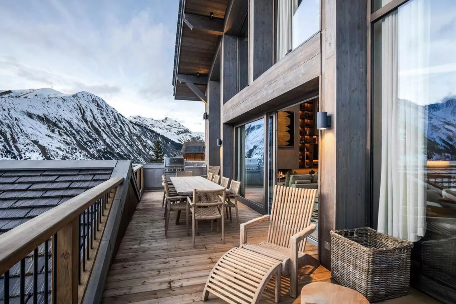 Un balcón de madera con asientos al aire libre ofrece vistas a montañas nevadas.