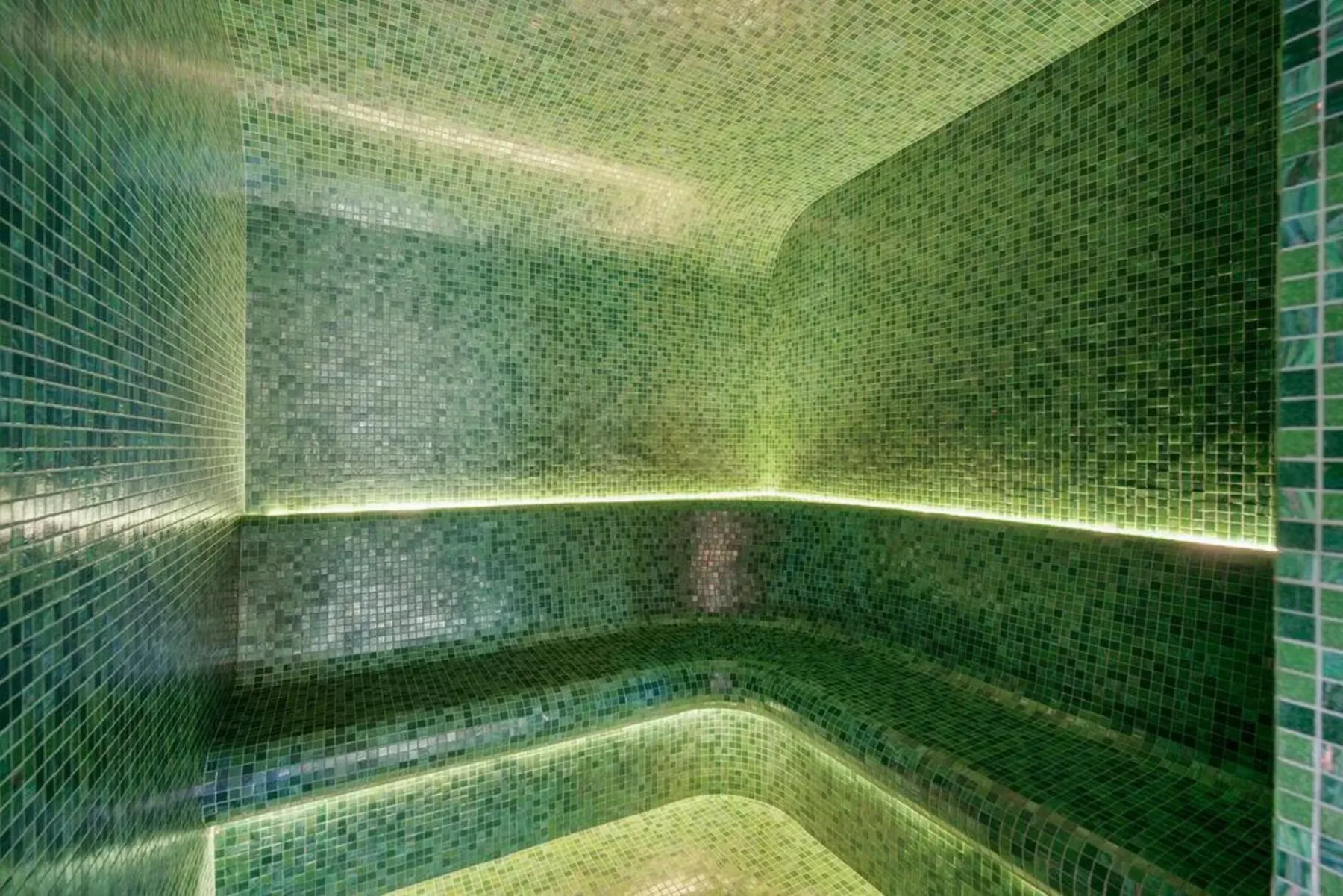 Un baño de vapor revestido de mosaicos verdes y con iluminación tenue.