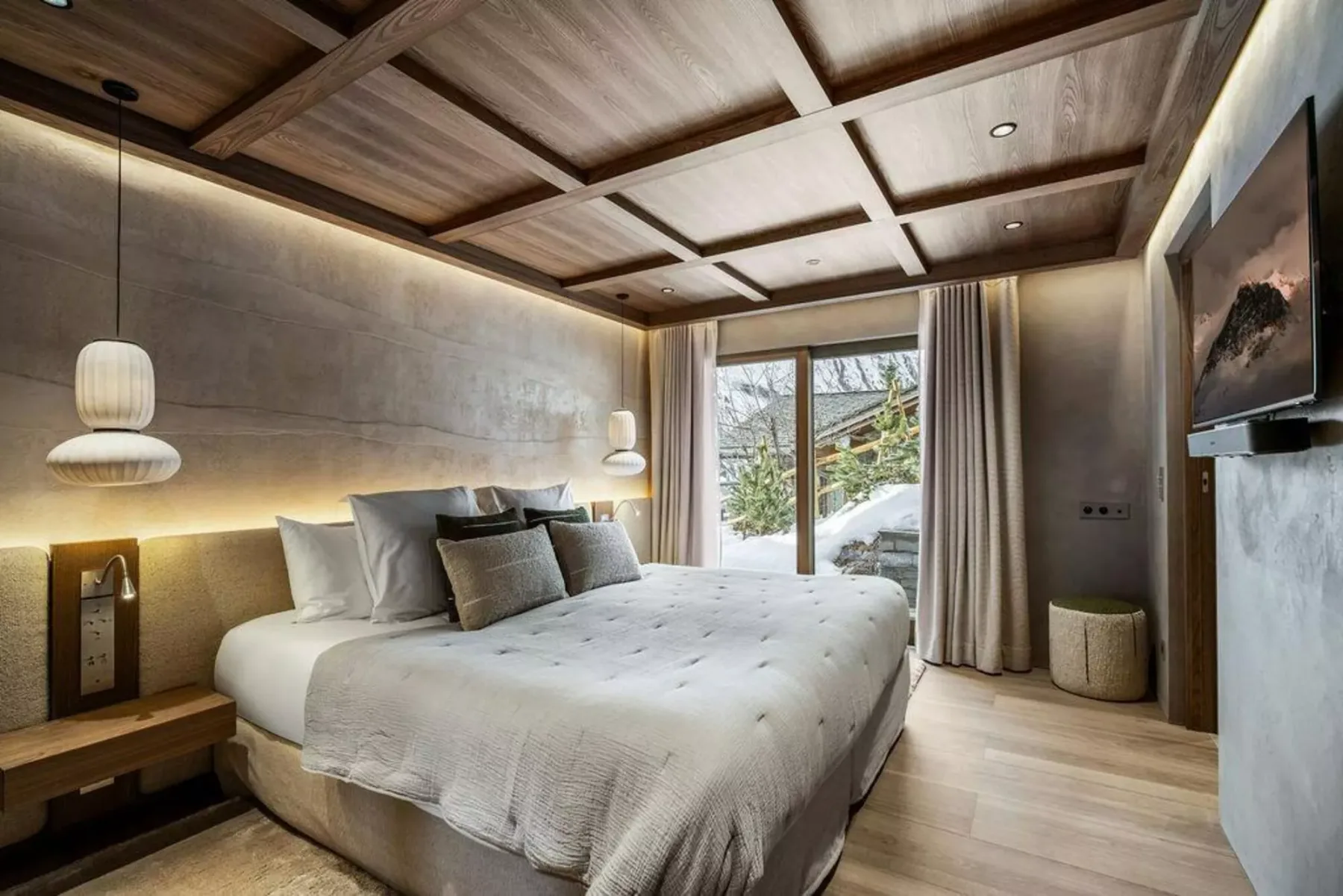 Un dormitorio con una cama grande, iluminación junto a la cama y una ventana con vistas a un paisaje nevado.
