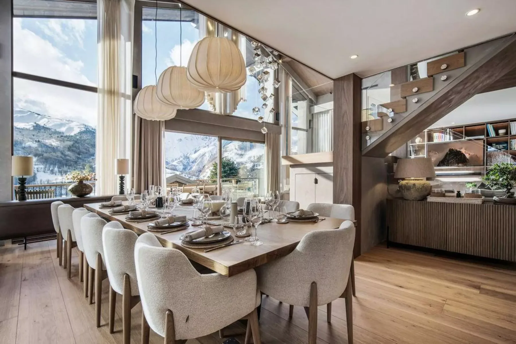 Comedor con una mesa larga y grandes ventanas con vistas a un paisaje montañoso.