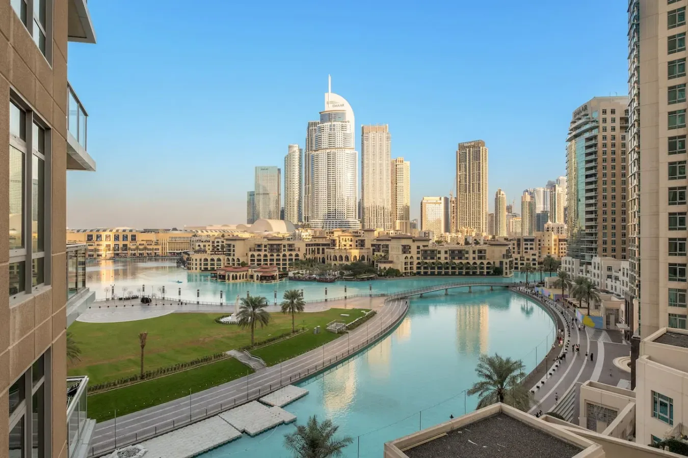 Un horizonte urbano se alza detrás de una zona verde junto al agua y una piscina curva.