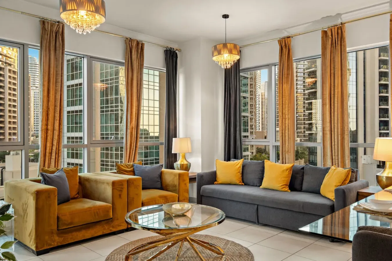 Una sala de estar luminosa con asientos junto a grandes ventanas y lámparas colgantes cálidas.