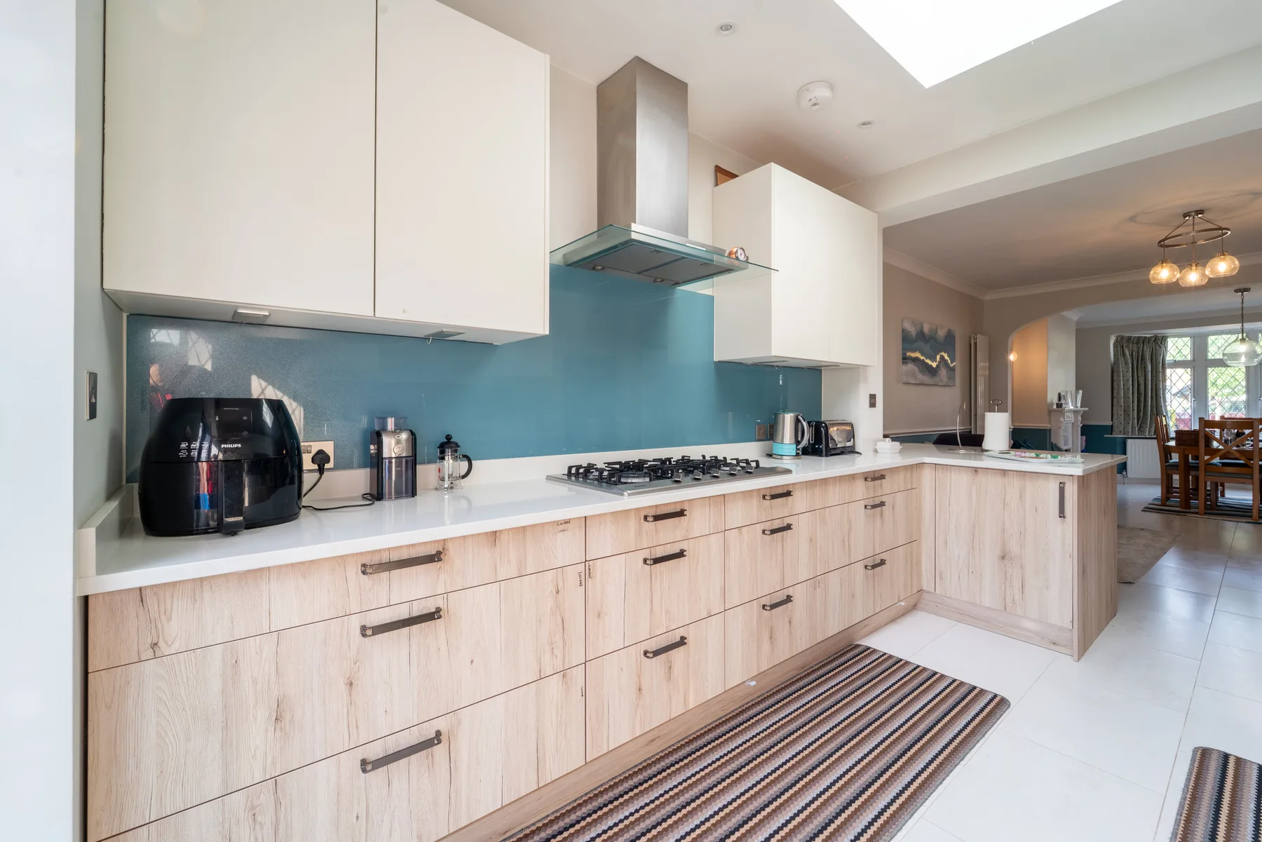 A bright modern kitchen with light wood cabinets and a blue backsplash.