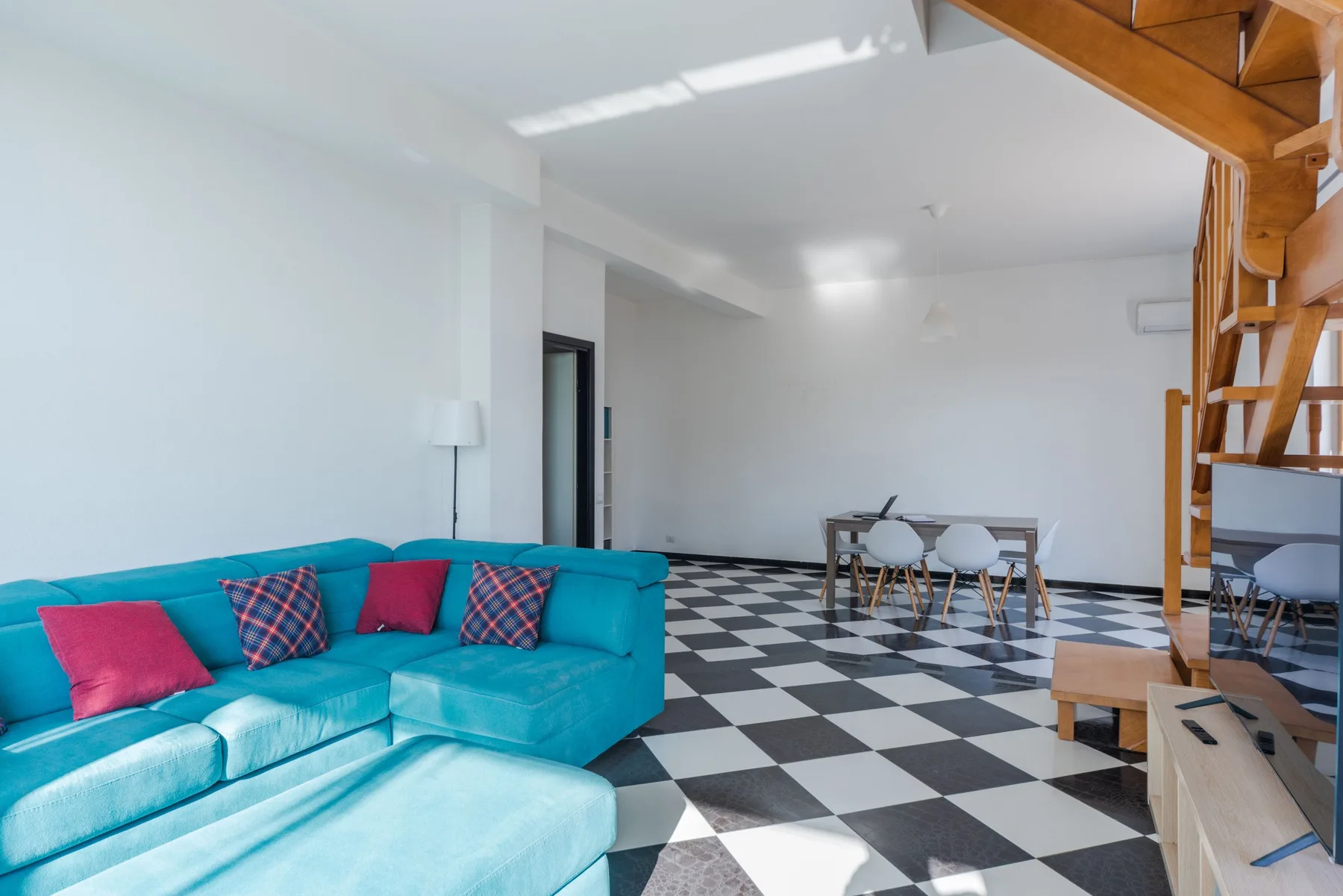 Una luminosa sala de estar y comedor con asientos turquesa y suelo de cuadros blancos y negros.
