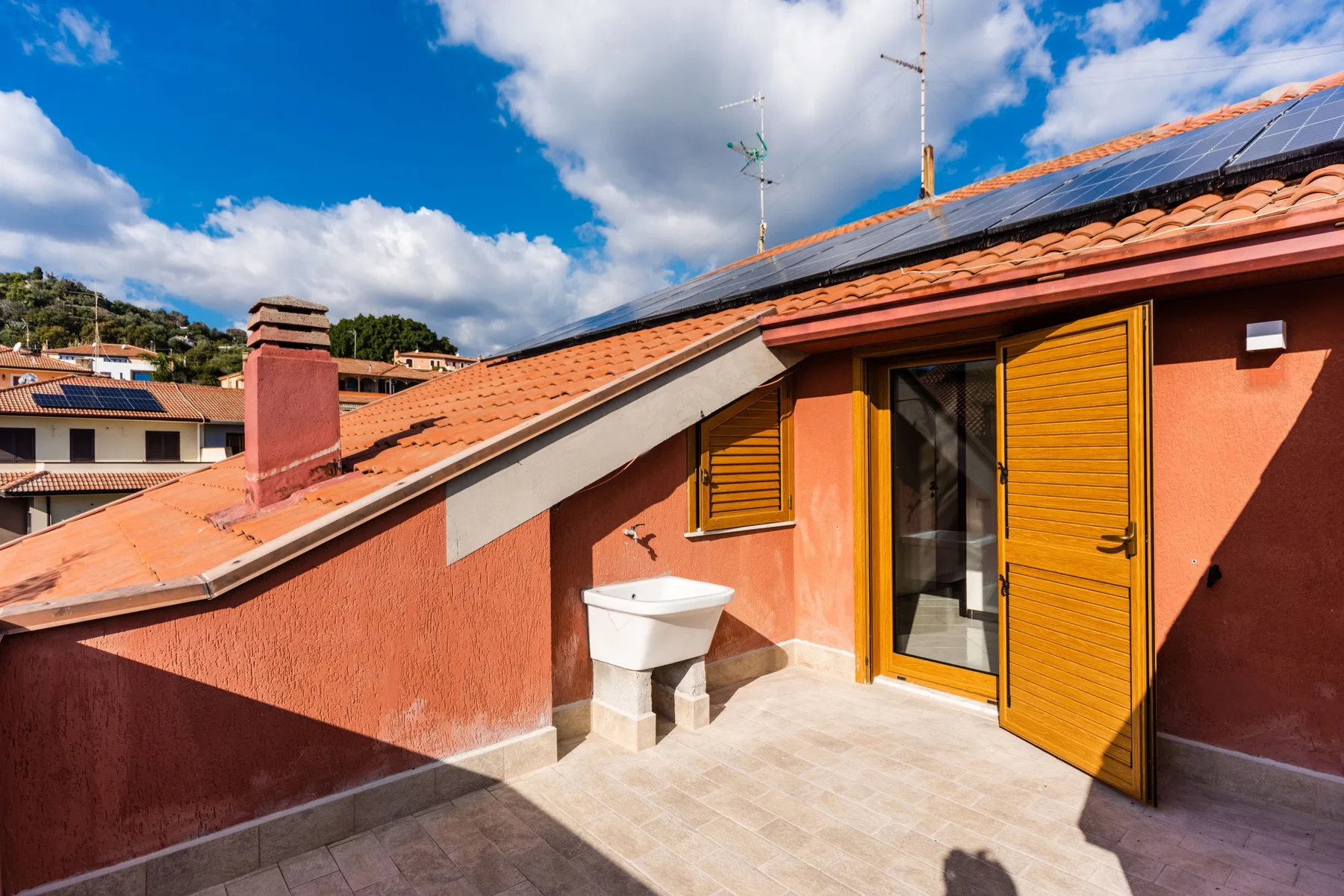 Una terraza soleada en la azotea con una puerta abierta y un pequeño lavabo junto a la pared.