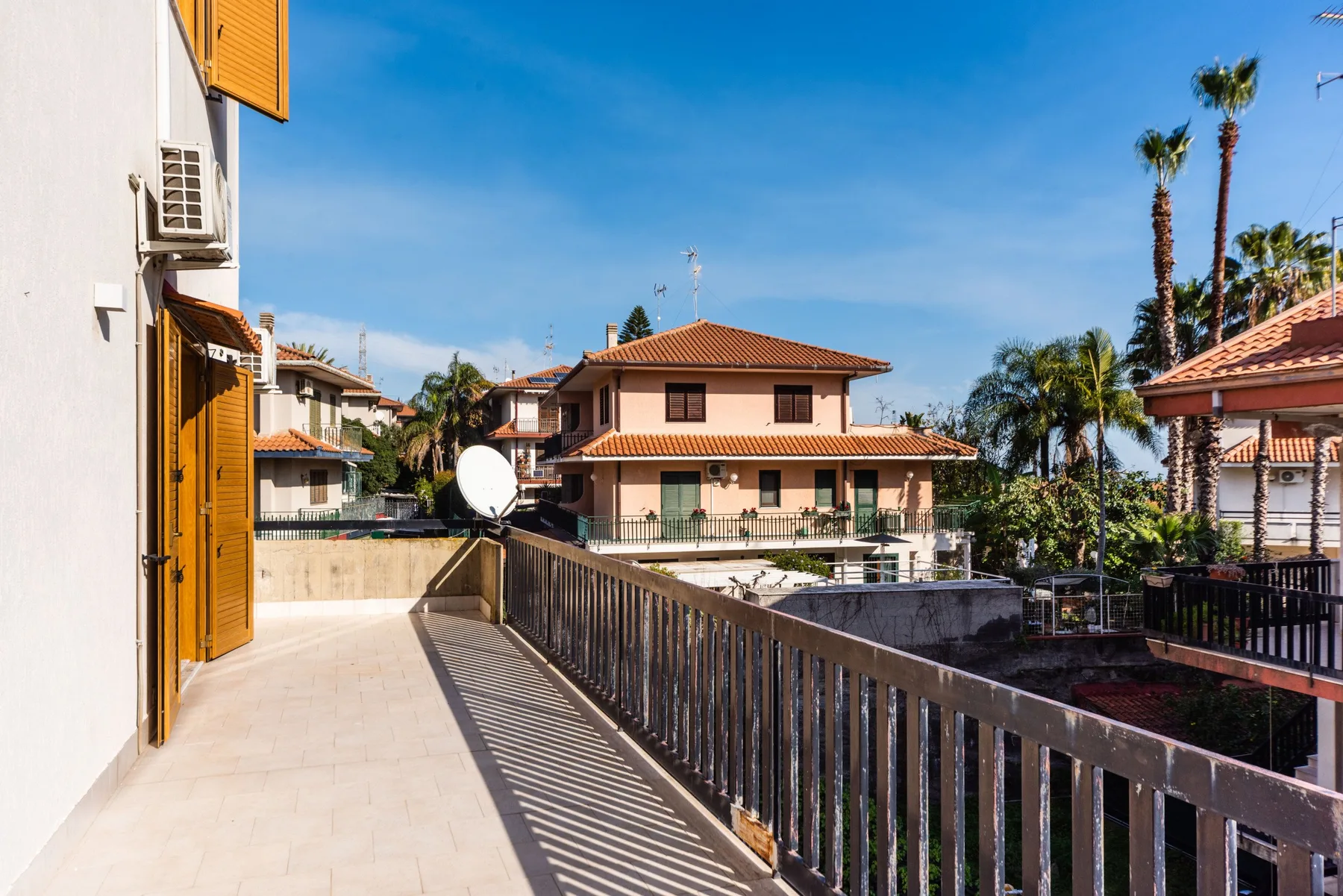 Un balcón soleado da a casas vecinas y palmeras.
