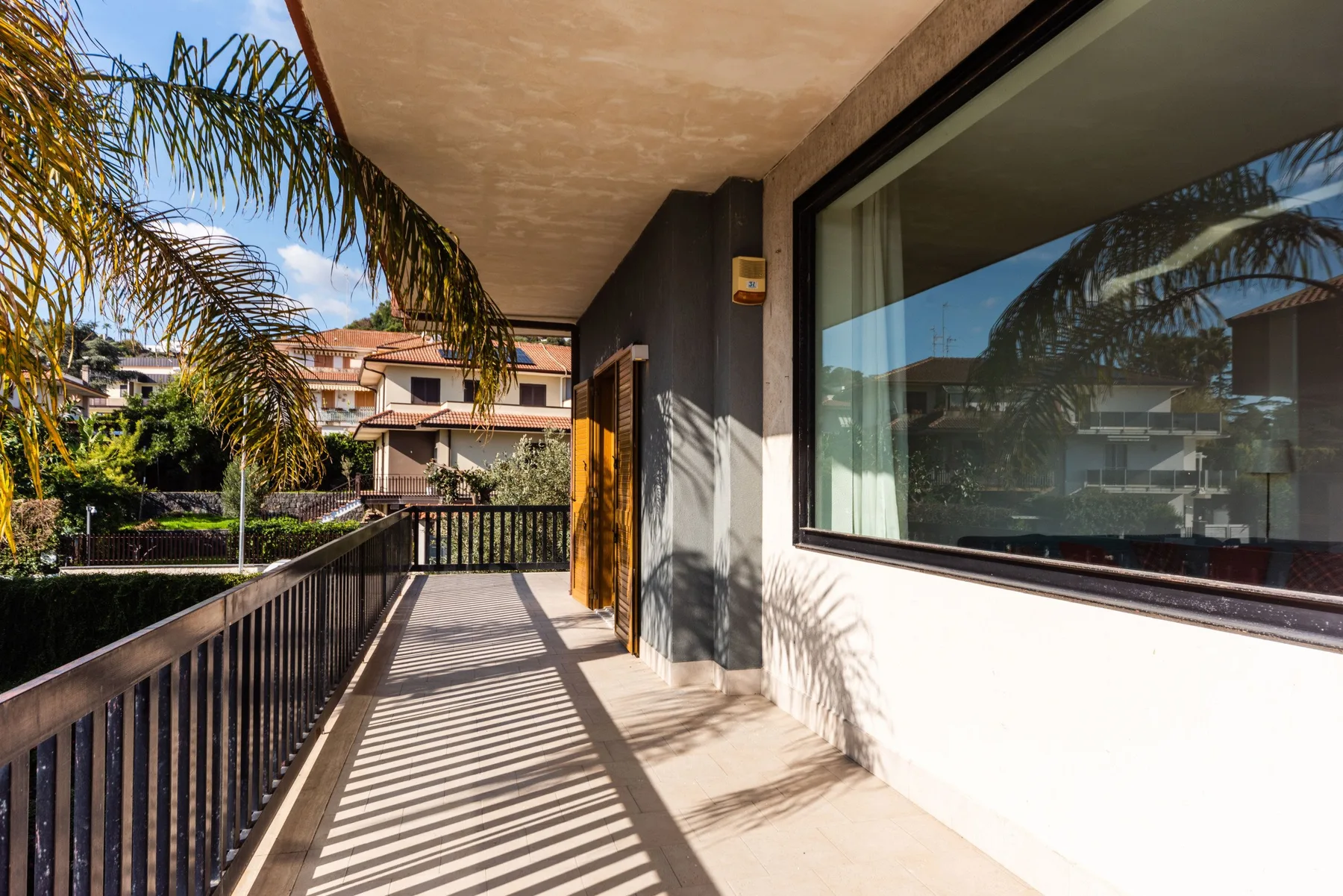 Un balcón exterior soleado con una barandilla y una ventana grande en la pared.