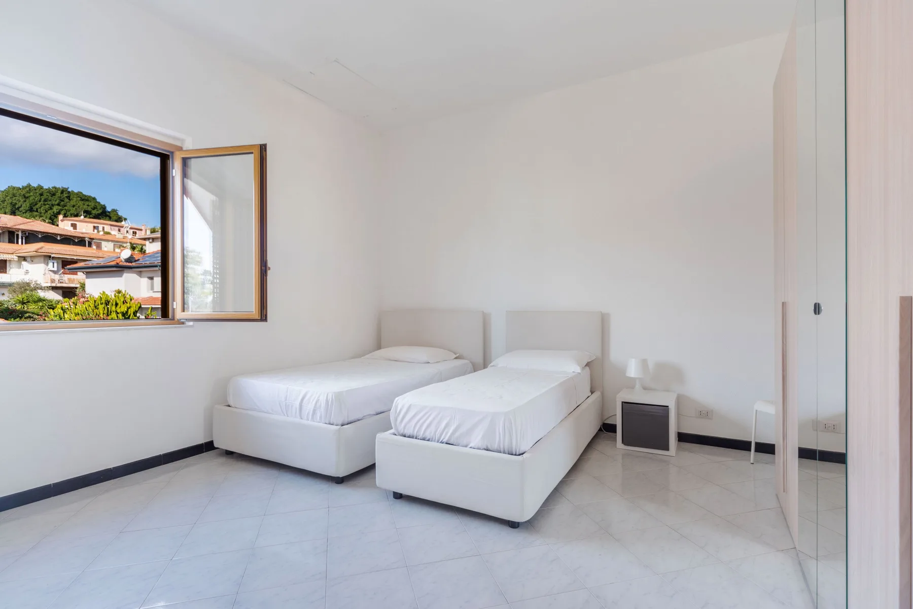 Un dormitorio luminoso con dos camas individuales y una ventana abierta.