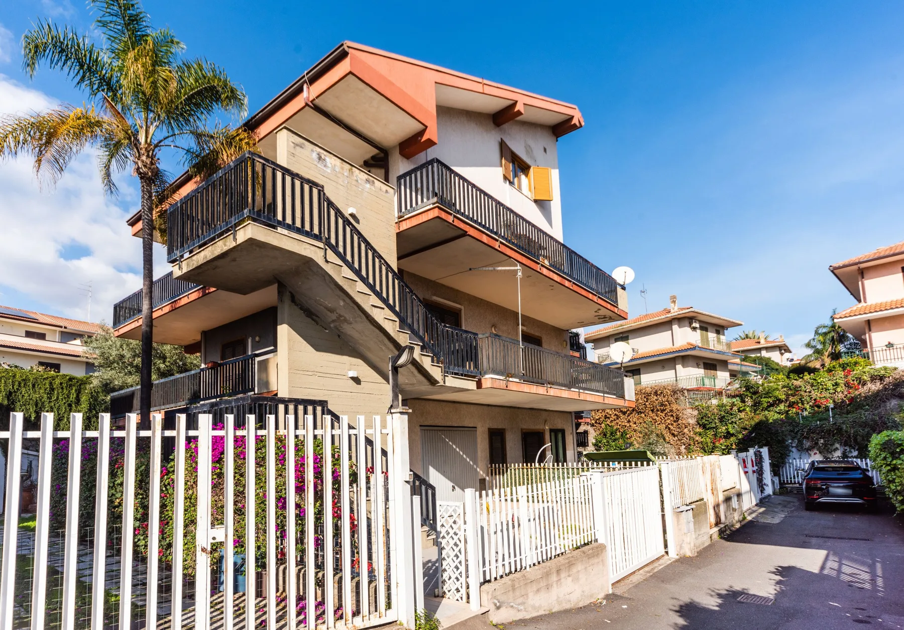 Un edificio residencial de varios niveles con balcones está junto a una entrada cercada.