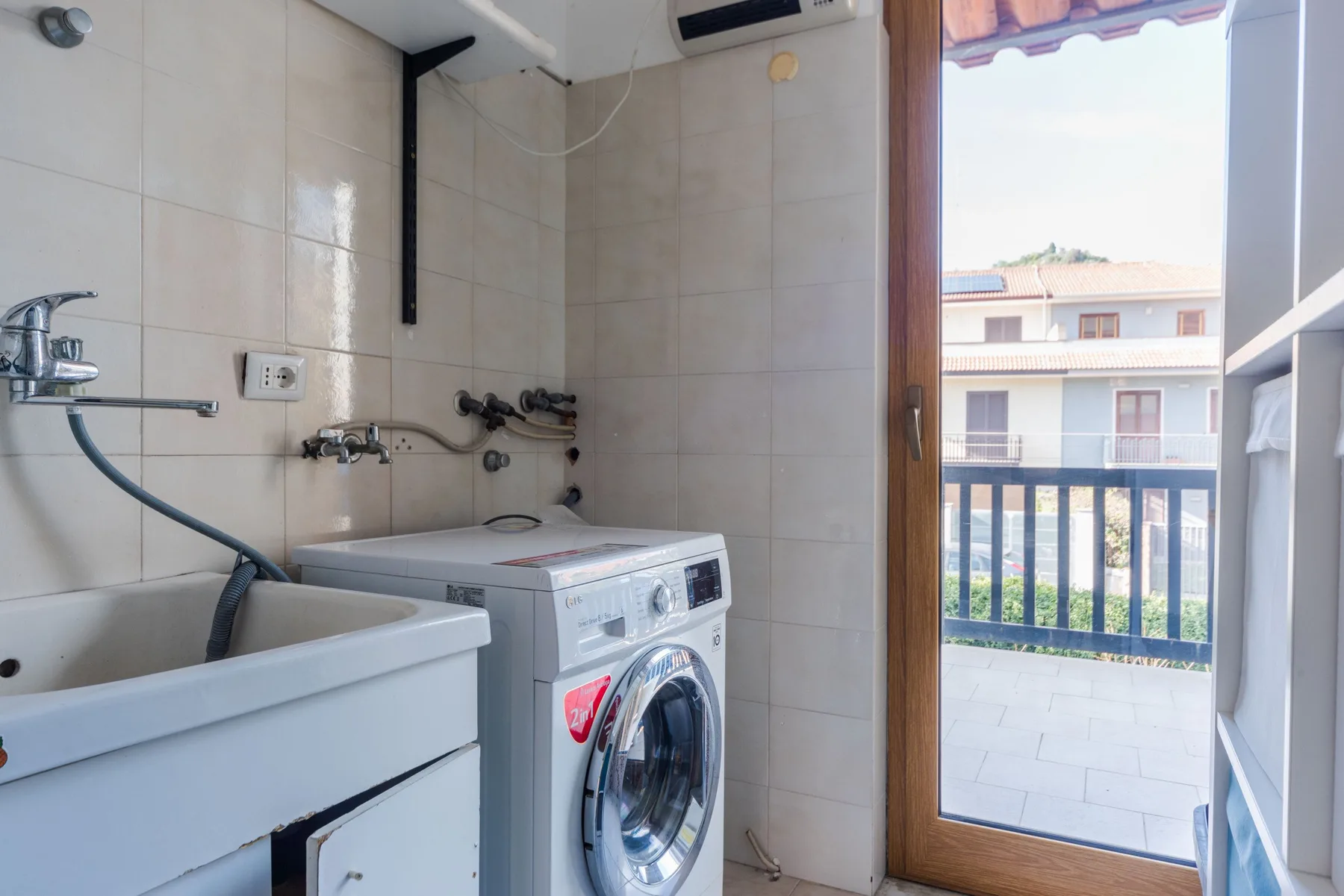 Zona de lavandería con una lavadora junto a una puerta abierta al balcón.