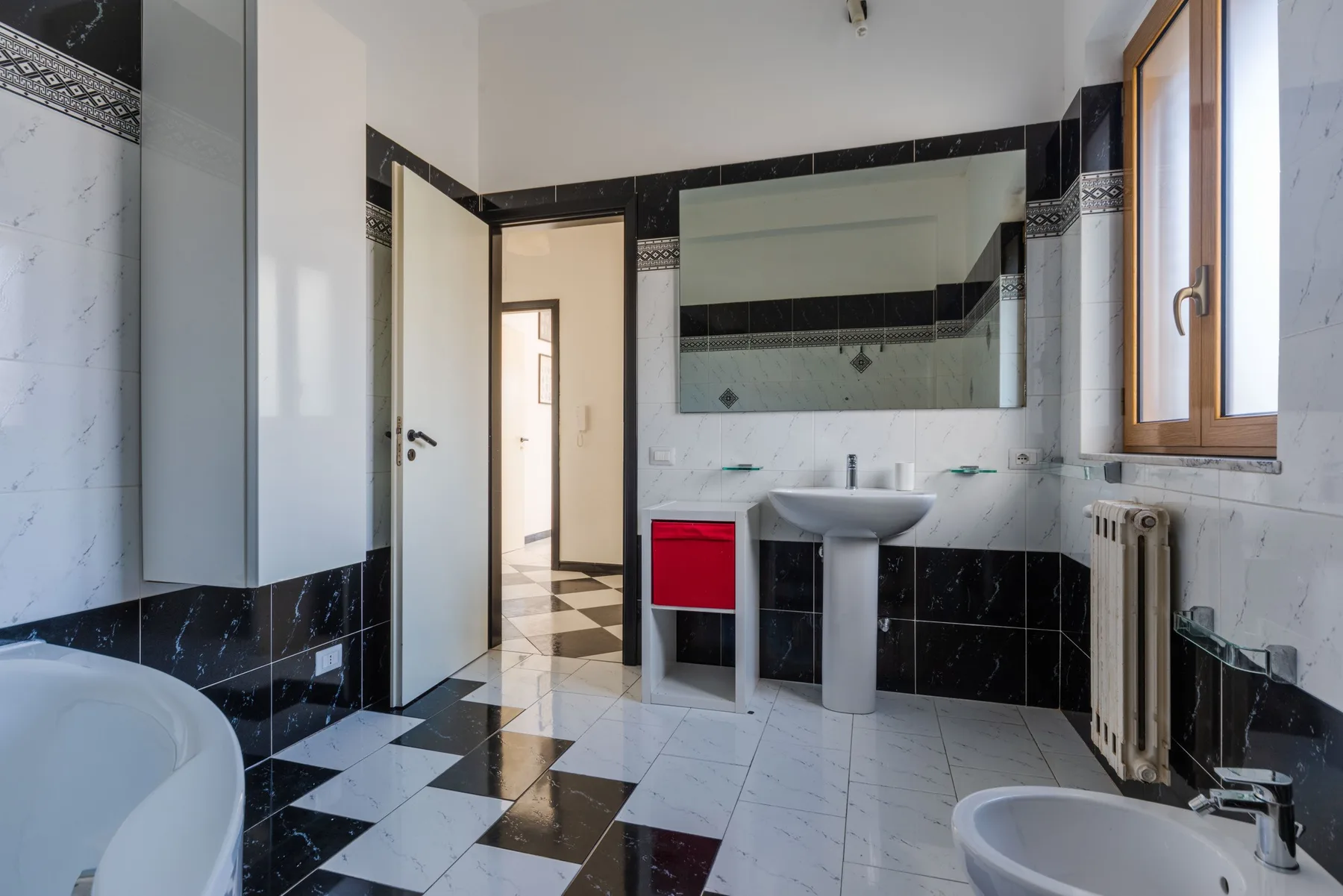 Un baño con azulejos, lavabo de pedestal y un espejo grande.