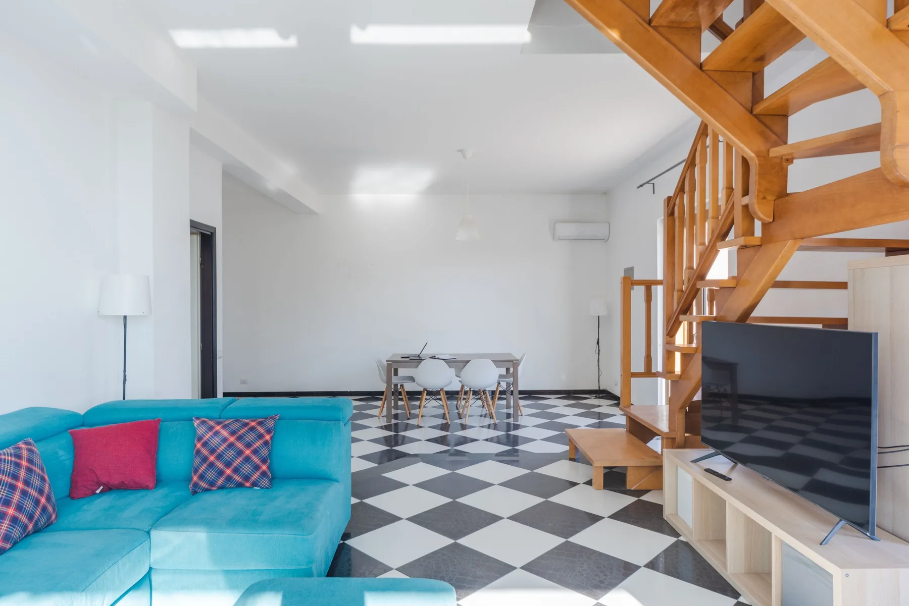 Una luminosa sala de estar y comedor con asientos turquesa, una mesa y una escalera de madera.