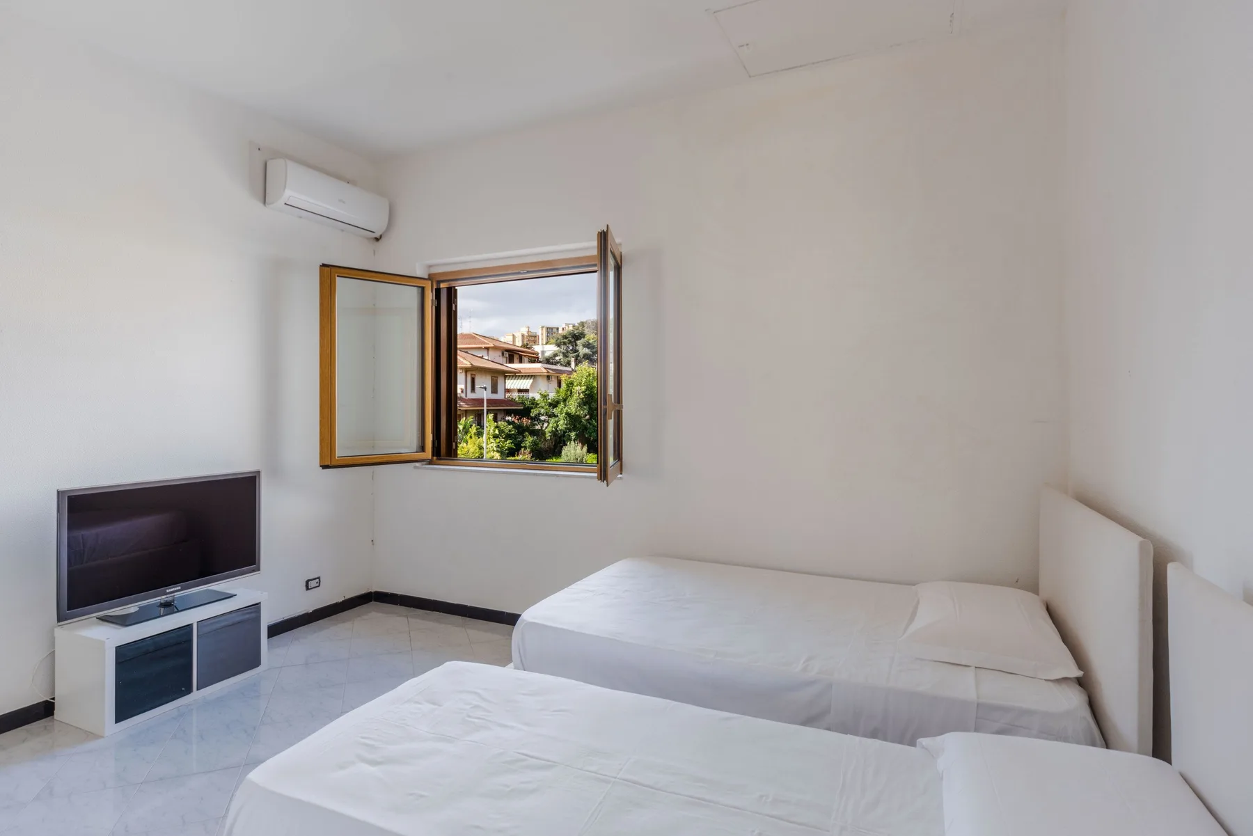Un dormitorio luminoso con dos camas y una ventana abierta con vistas a la vegetación.