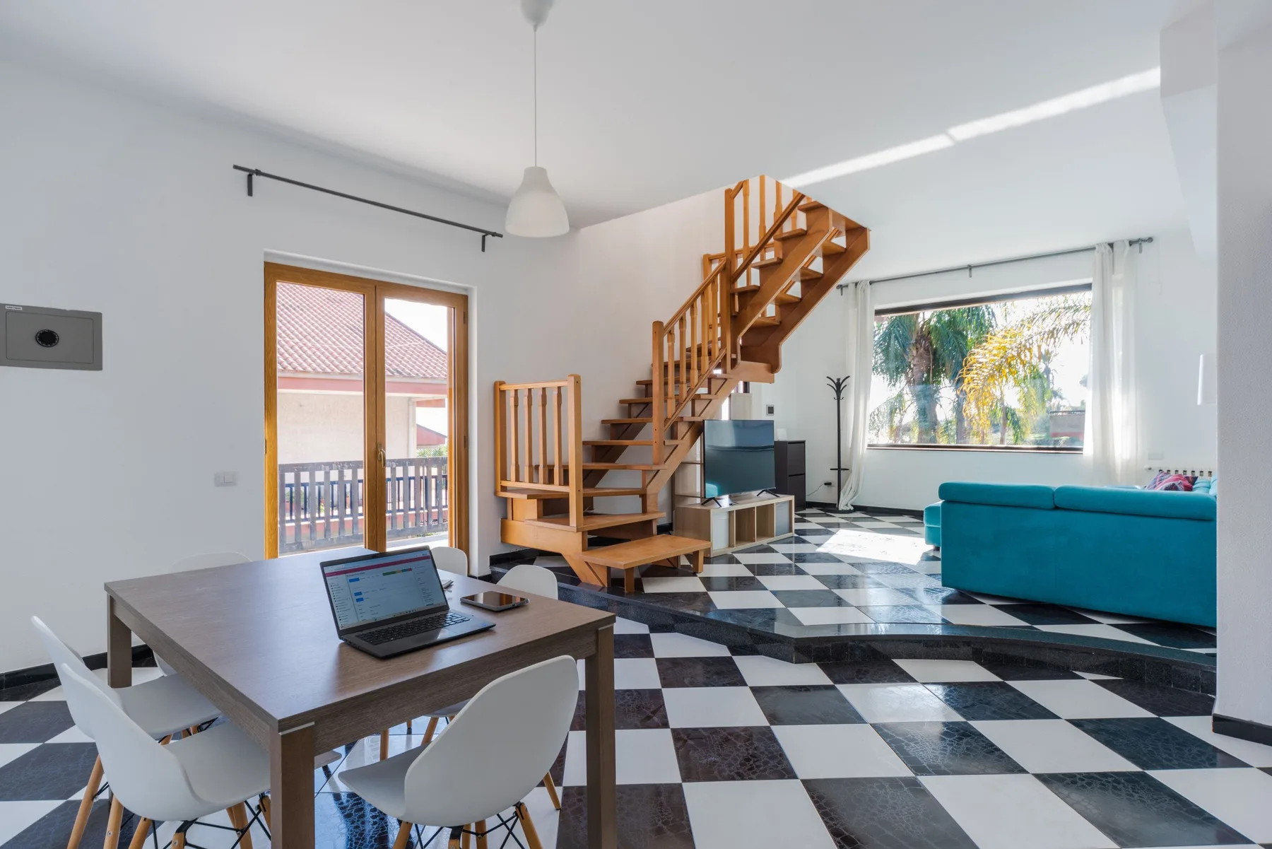 Una luminosa sala de estar y comedor con una escalera de madera y ventanas grandes.