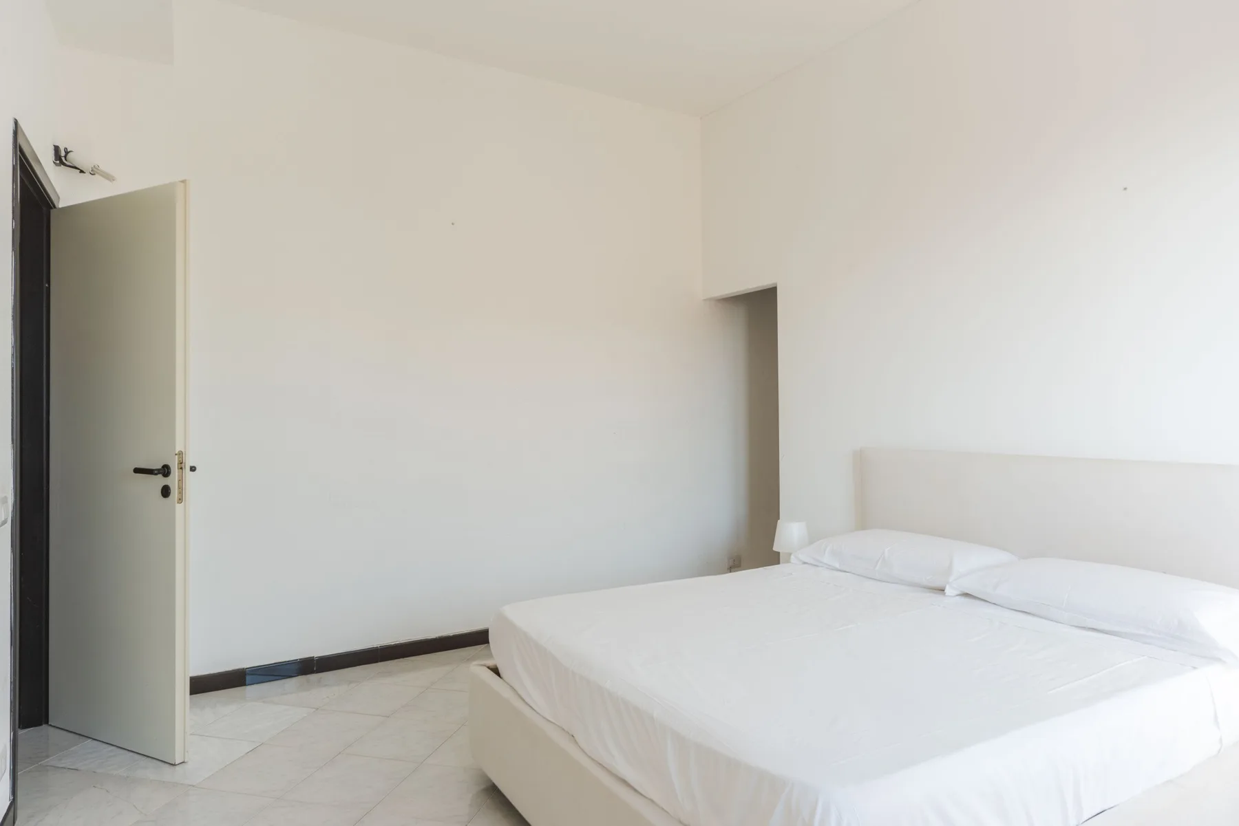 Un dormitorio luminoso con ropa de cama blanca y una puerta abierta.