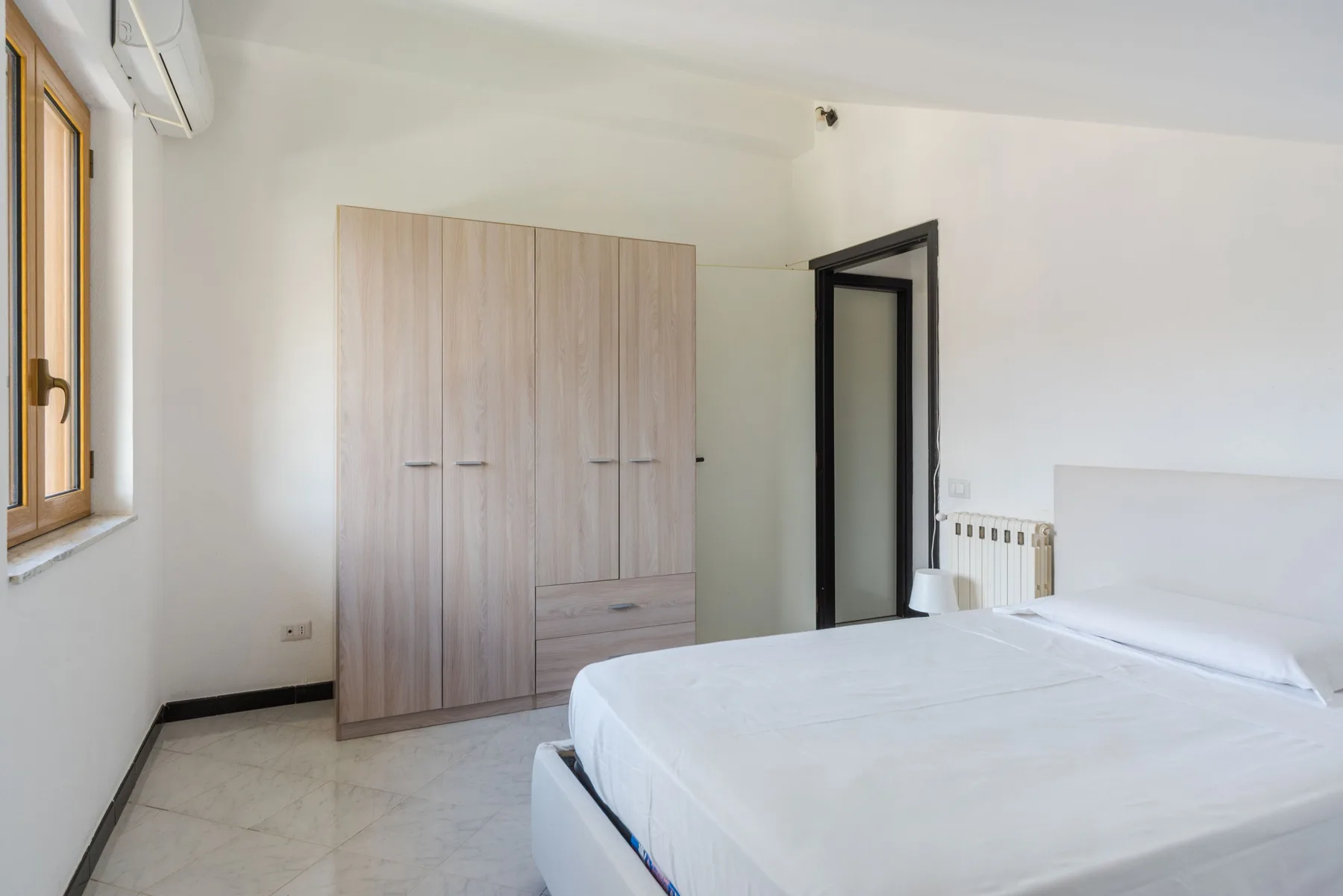 Un dormitorio luminoso con una cama, un armario y una puerta abierta.