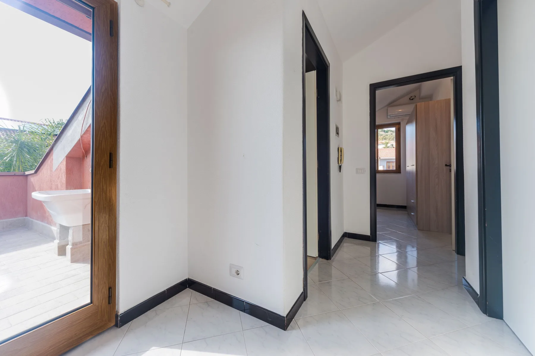 Un pasillo luminoso con suelo de baldosas da a una habitación con ventana.
