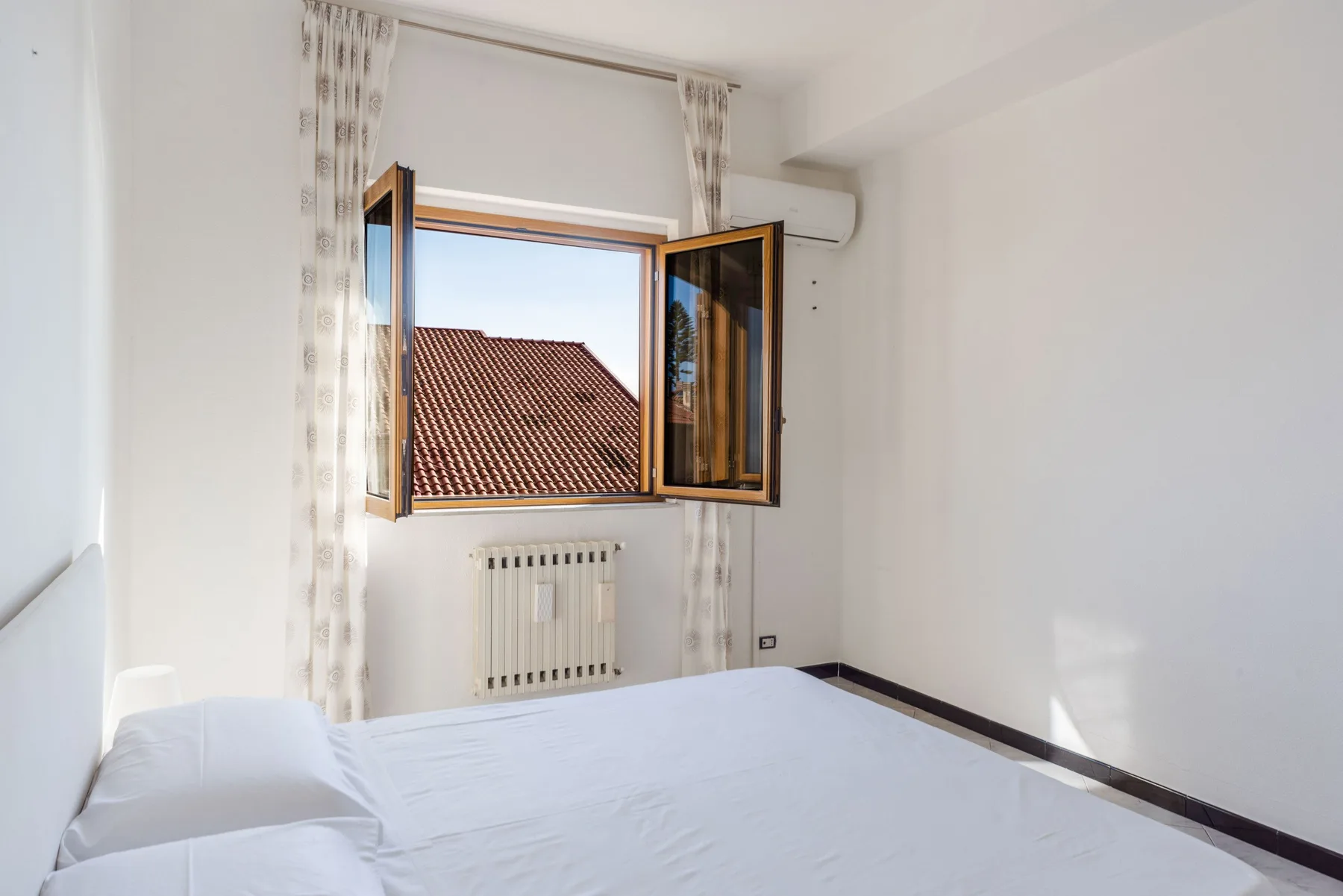 Un dormitorio luminoso con ropa de cama blanca y una ventana abierta.