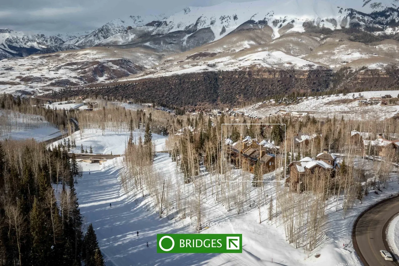 A snow-covered mountain valley with a winding road and scattered buildings.