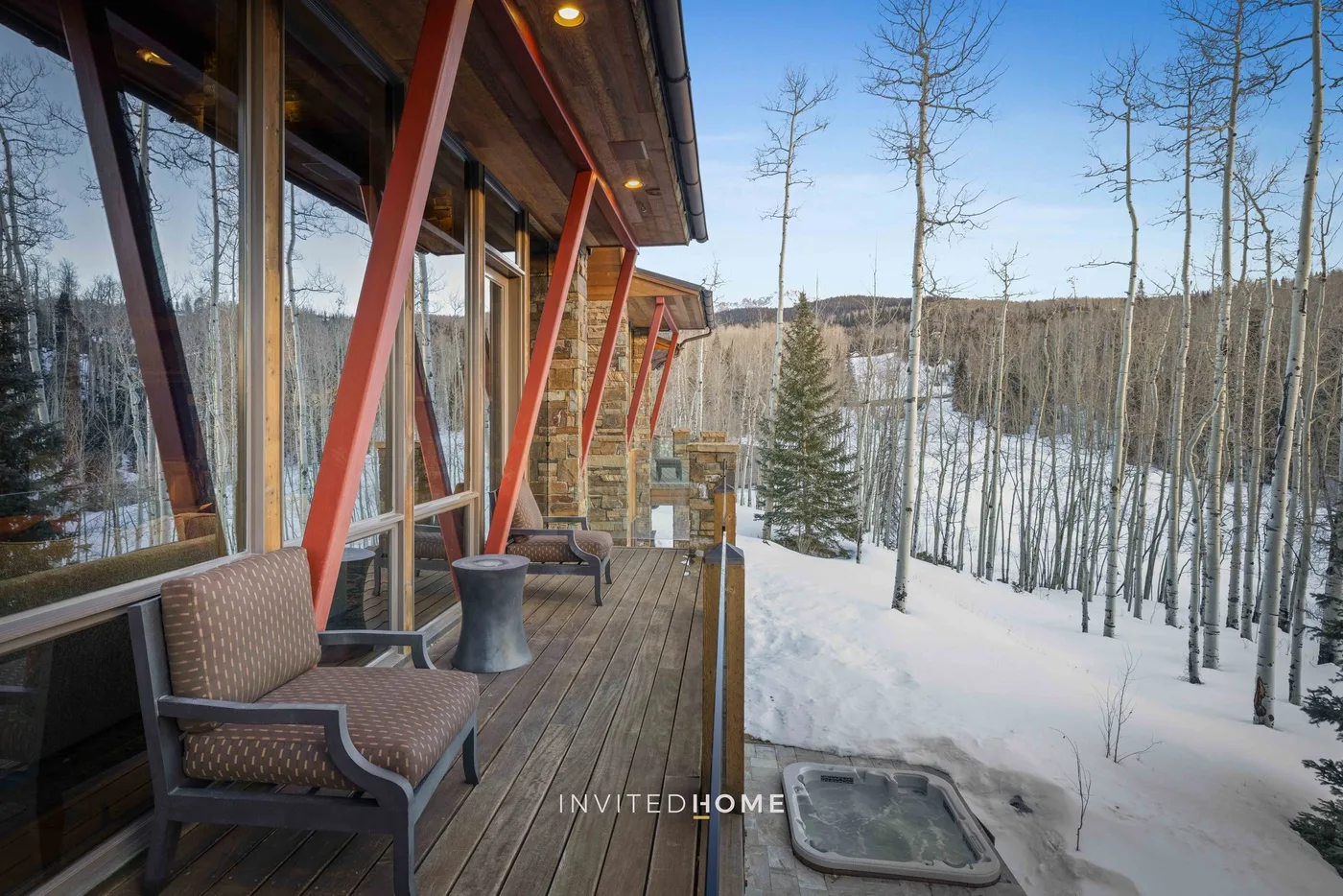 A wooden deck with outdoor seating overlooks a snow-covered wooded landscape.